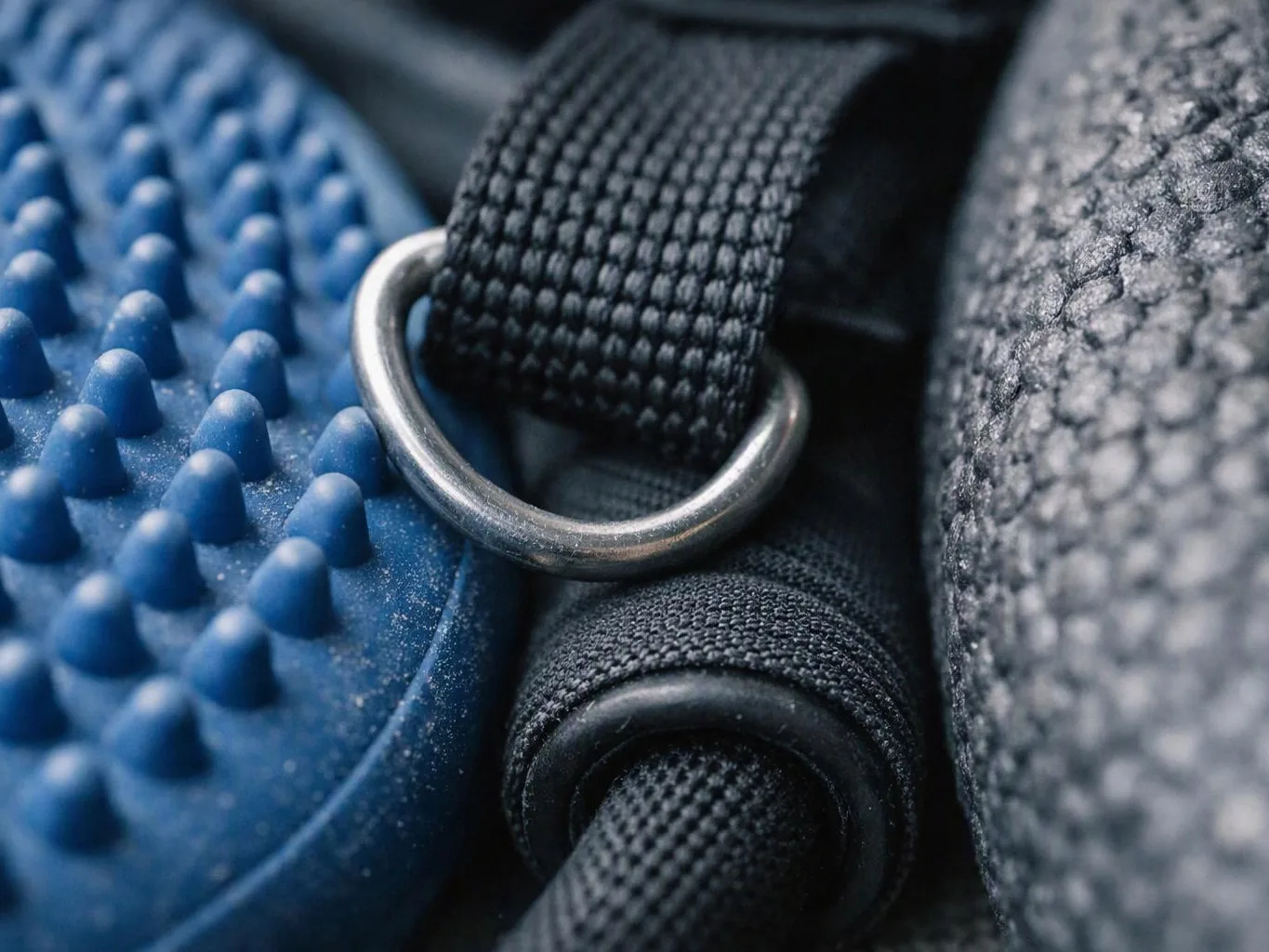 Close-up of a blue textured rubber surface beside black woven straps and a metal ring