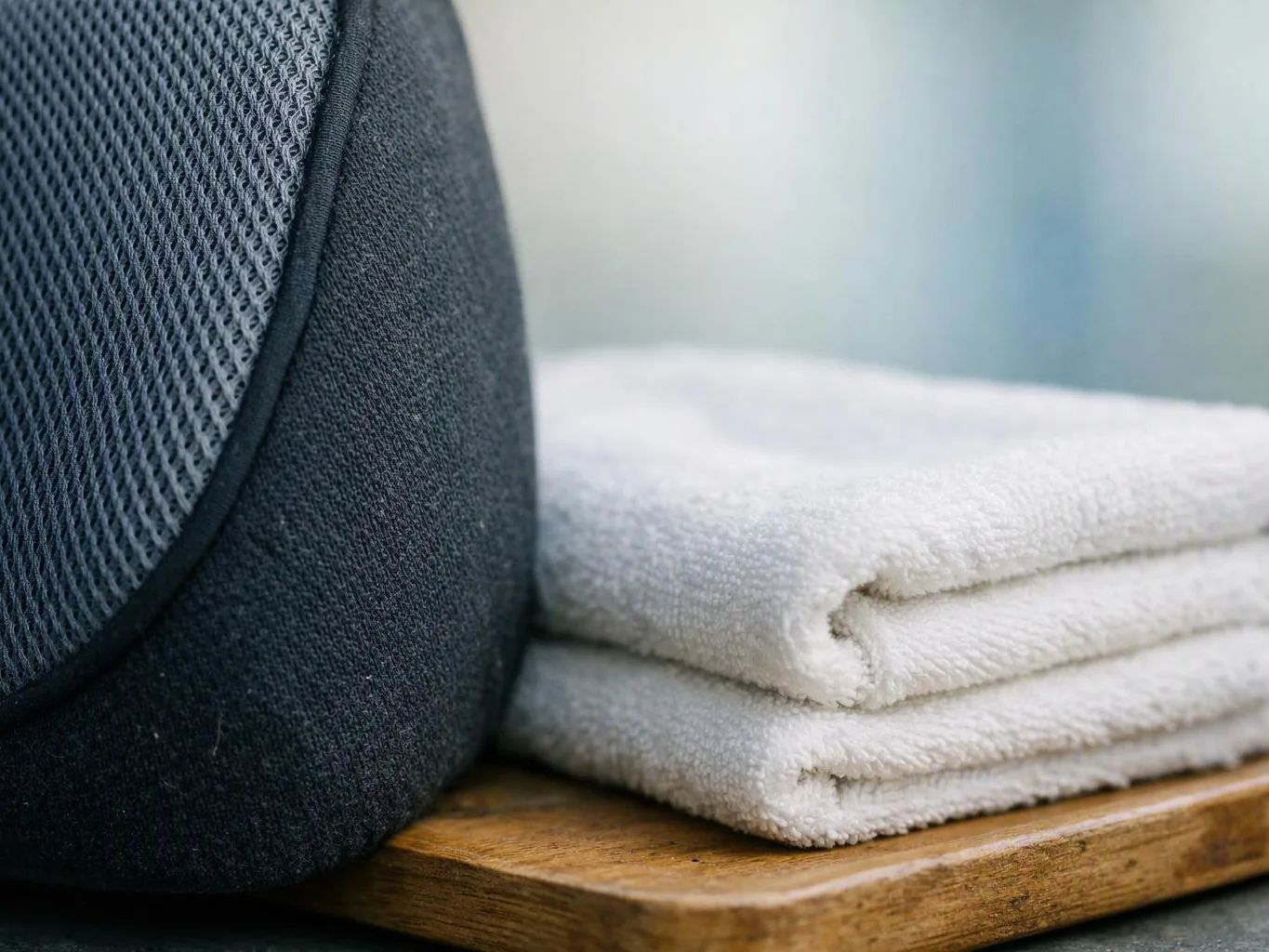 A dark fabric bag sits beside two folded white towels on a wooden tray