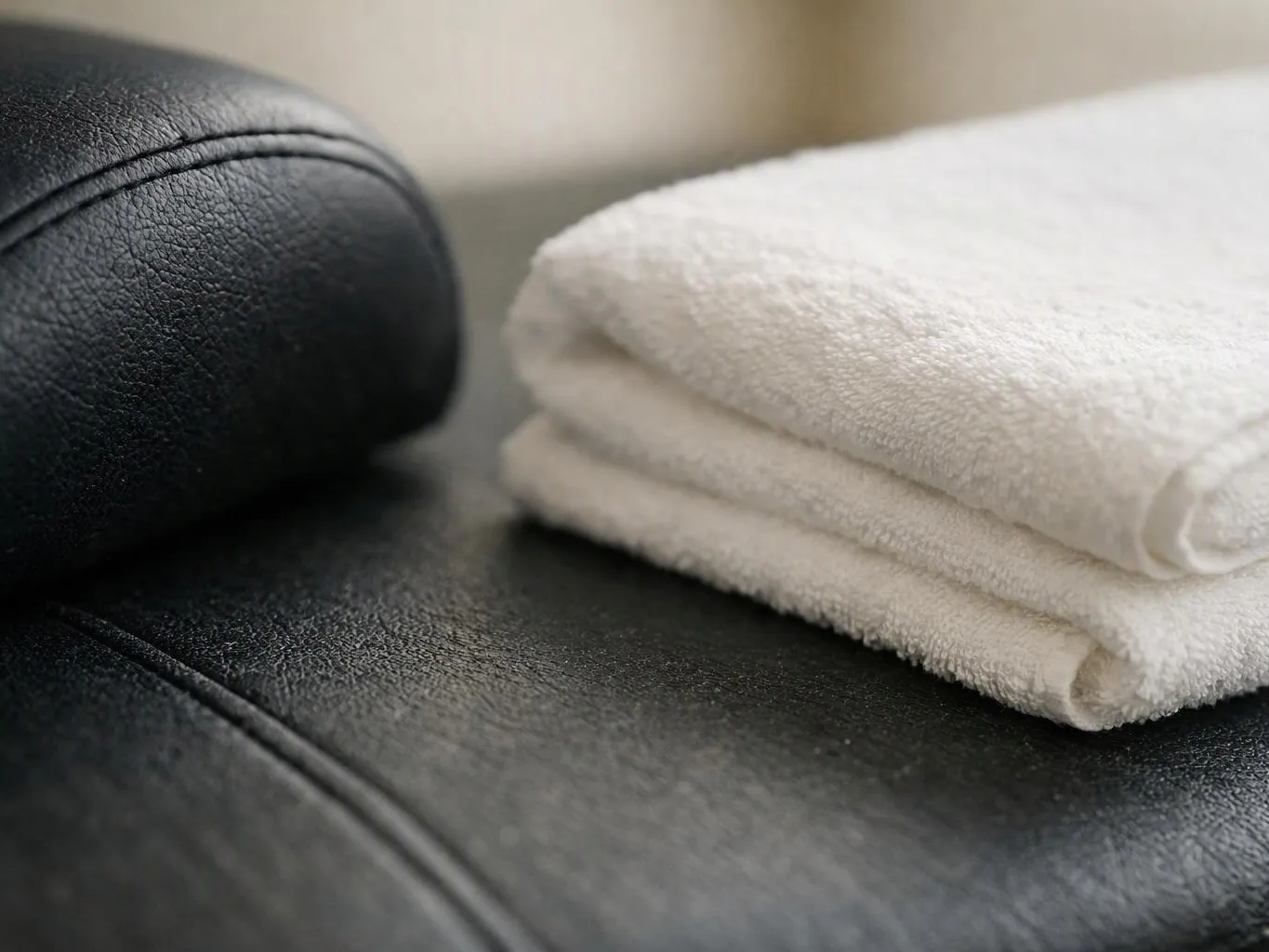 Folded white towels rest on a black leather surface in soft indoor light