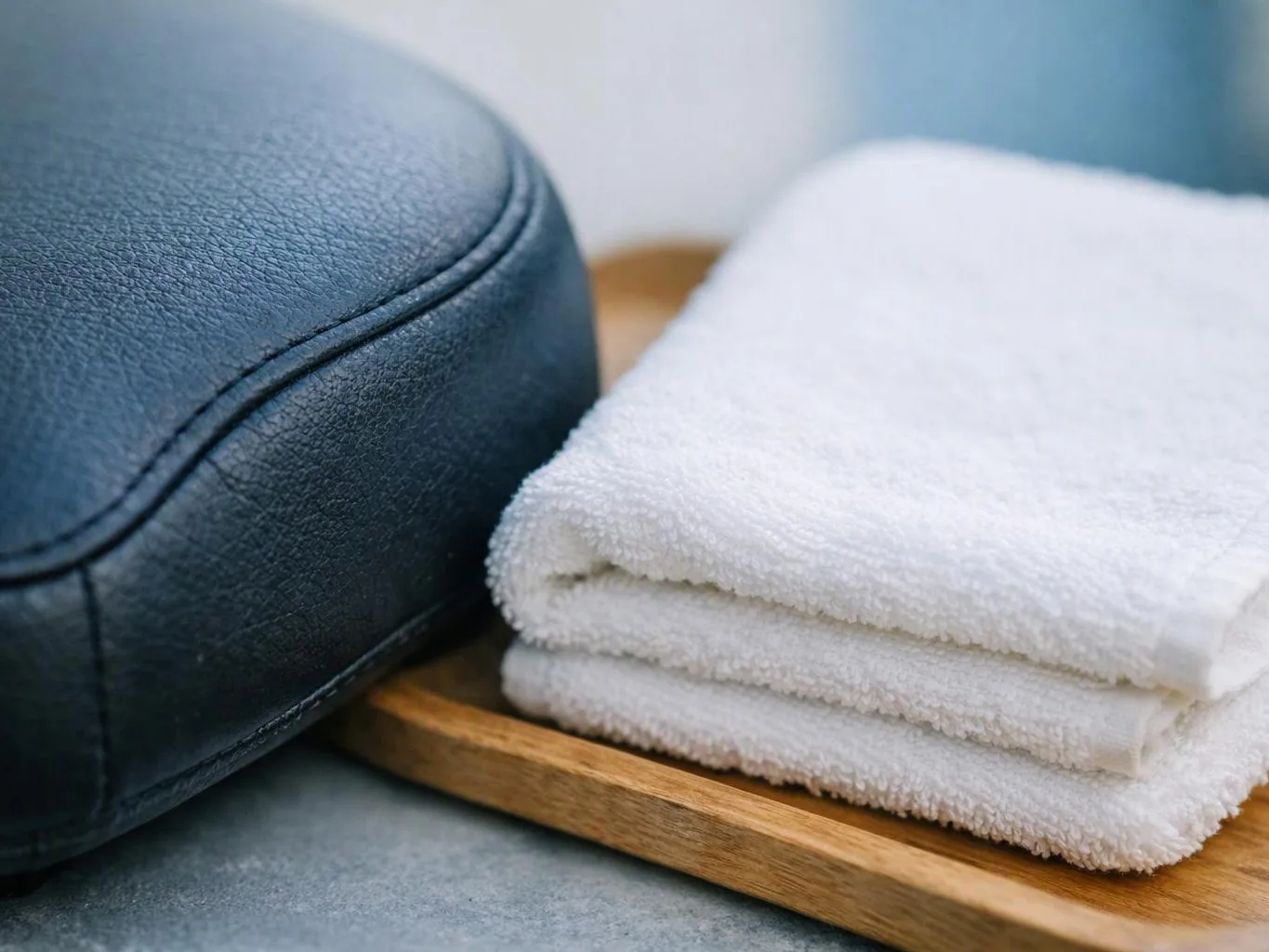 Folded white towels rest on a wooden tray beside a dark leather cushion