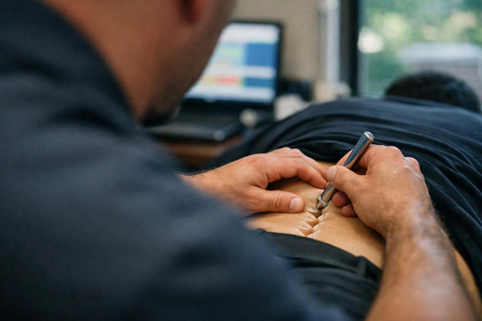 A person uses a metal tool to examine another person’s abdomen in a clinic room