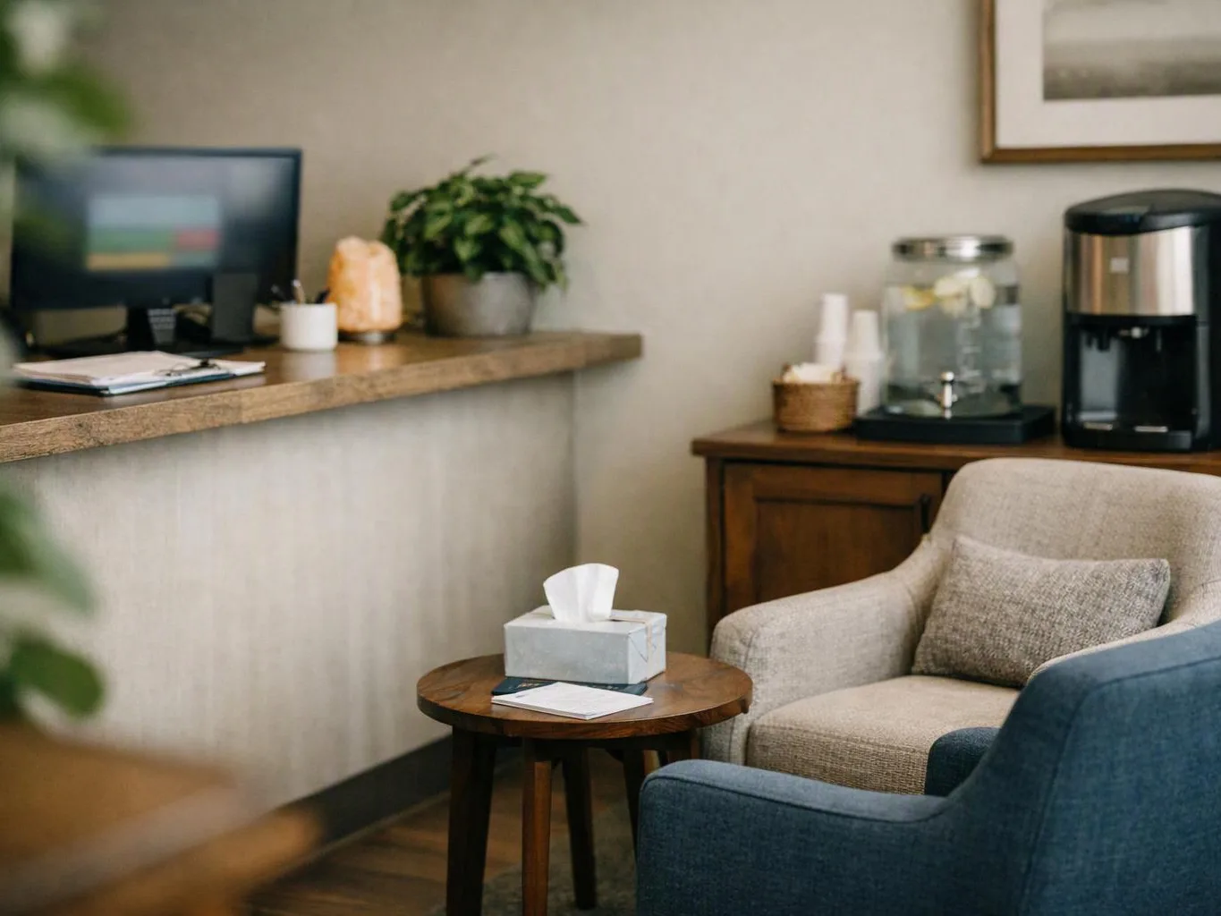 A quiet office lounge shows a chair, side table with tissues, desk, plants, and coffee machine