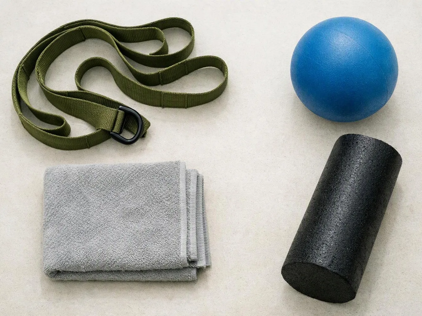 A yoga strap, blue exercise ball, folded gray towel, and black foam roller sit on a light floor